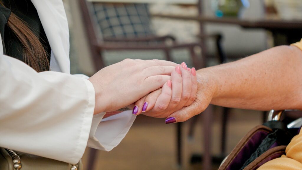 two women with painted nails hold hands at a skilled nursing facility