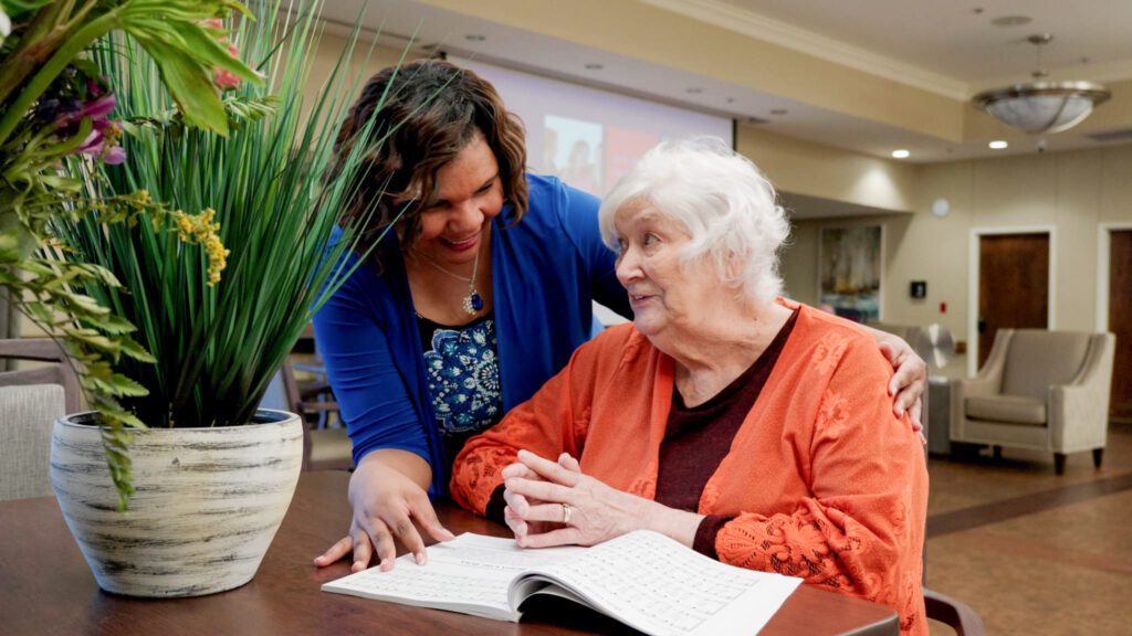 A staff worker and woman smile and talk at a skilled nursing facility